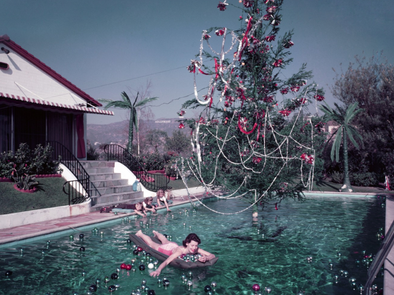 A photo by Slim Aarons of a woman in a swimming pool with a Christmas tree.